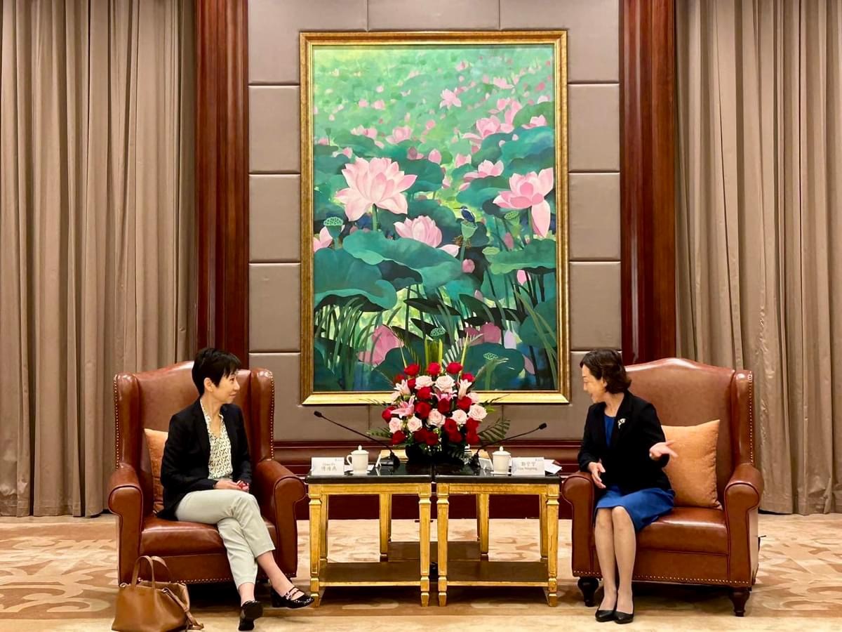 Two women sit in leather chairs facing each other, with a lotus flower painting behind them.